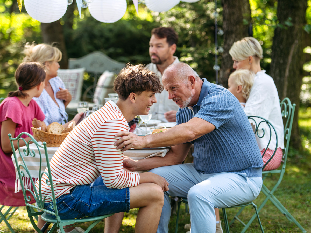 boy talking to an elderly man outside at a table